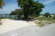 The back has a view of the inlet. The front is open to the street. There is a gravel drive in the center of the site. The right side of it has a small street that runs next to it. There is a picnic table under a tree on the right.