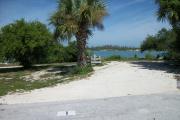 The back has a view of the inlet. The front is open to the street. There is a gravel drive in the center and a grassy area on the right and left sides. The left side of it has a palm tree. There is a palm tree and a cedar tree on the right.