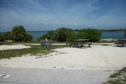 The back has a view of the inlet. The front is open to the street. There is a gravel drive in the center of the site. The left side has a picnic table with a fire ring next to it.