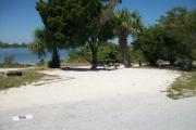 The front is open to the street.  The back has a large cedar, palm trees, and gumbo-limbos behind it. The front is open to the street. The left side has a fire ring on it. The picnic table is nestled between a cedar and a palm tree at the back of the site.