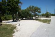 The back has a view of the inlet. The front is open to the street. There is a gravel drive in the center. The right and left sides of the site have a variety of trees. There is fire ring on the left. A picnic table is at the back of the site.