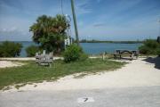 The back has a view of the inlet. The front is open to the street. There is a gravel drive in the center of the site. There is a picnic table with fire ring behind it on the left.