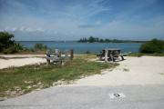 The back has a view of the inlet. The front is open to the street. There is a gravel drive in the center of the site. The left side has picnic table. The right side has a small grassy area.