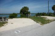 The back has a view of the inlet. The front is open to the street. There is a gravel drive in the center of the site. There is a picnic table on the left and a small grassy area on the right.