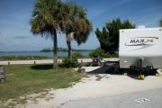 The back has a view of the inlet. The front is open to the street .There is a gravel drive in the center of the site. There are two sable palms next to a picnic table on the left. A white RV sits in the driveway.