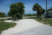 The back has a view of the inlet. The front is open to the street. There is a gravel drive in the center of the site. A picnic table sits in front of a sea grape on the left.  There is a fire ring on the far left.  Two sable palms are on the right.