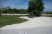 The back has a view of the inlet. The front is open to the street. There is a gravel drive in the center of the site. The left side has a picnic table in front of a sea grape tree and a fire ring.