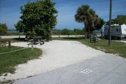 The back has a view of the inlet. The front is open to the street. There is a gravel drive in the center of the site.  There is a picnic table in front of a large sea grape tree on the left. There are two stately palms on the right.
