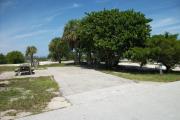 The campsite is handicap accessible. The front is open to the street and the back faces a street. There is a gravel drive in the center of the site. The left side has a wheelchair accessible picnic table. The right side has several trees.