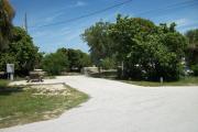 The campsite is handicap accessible. The front is open to the street.  The back faces a street. There is a gravel drive in the center and a grassy area on the right and left sides. The right has a several trees. A picnic table is on the left.