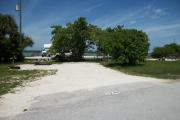 The front is open to the street and the back faces a street. There is a gravel drive in the center of the site. There is a fire ring on the left side of the site, and a picnic table at the back. There are sea grapes in the far right corner.