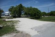 The front is open to the street and the back faces a street.  There is a gravel drive in the center of the site. The right has a grassy area with sea grapes. There is a fire ring at the far left of the site and a picnic table at the back.