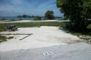 The front is open to the street and the back faces a street. There is a gravel drive in the center of the site. The left side has a picnic table with a fire ring next to it.  A large sea grape is on the right.
