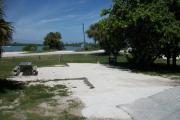 The front is open to the street. The back faces a street. There is a gravel drive in the center of the site. The right side has large sea grape. There is picnic table on the left.