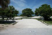 The front is open to the street and the back faces a street. There is a gravel drive in the center of the site. There is a picnic table with a fire ring behind it on the left and a sea grape tree on the right.