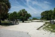 The front is open to the street and the back faces a street. There is a gravel drive in the center of the site. The left side has a picnic table next to trees and palms.