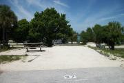 The front is open to the street and the back faces a street. There is a gravel drive in the center of the site. The left side has a picnic table and a fire ring in front of a large sea grape tree.