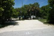 The front is open to the street and the back faces a street. There is a gravel drive in the center of the site. A picnic table is on the left side shaded by sea grapes. A fire ring is at the back of the site. Trees surround the site.