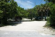 The front is open to the street and the back faces a street. There is a gravel drive in the center of the site. The left side has a picnic table in front of a large sea grape. There is a fire ring at the back of the site.