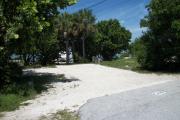 The front is open to the street and the back faces a street. There is a gravel drive in the center of the site. The site has a variety of trees. There is a fire ring at the back.
