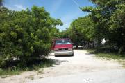 The front is open to the street and the back faces a street. There is a gravel drive in the center of the site. There are trees surrounding the site. There is a red van in the driveway.