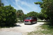 The front is open to the street and the back faces a street. There is a gravel drive in the center of the site. Trees surround the site. A red van sits in the driveway. A picnic table is on the left.