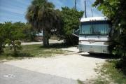 The front is open to the street and the back faces a street. There is a gravel drive in the center of the site. There is a large white RV in the driveway. There is a sea grape, gumbo-limbo, and a palm on the left. A sea grape is on the right.