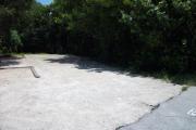 The front is open to the street. The back is densely packed with foliage. There is a gravel drive in the center of the site. The right side of the site has a row of large sea grape trees. A fire ring is on the left.