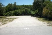 The front is open to the street. The back is filled with greenery. There is a gravel drive in the center of the site. A picnic table is on the right and a fire ring is on the left.