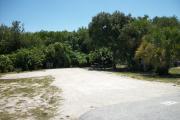 The front is open to the street. The back is filled with greenery. There is a gravel drive in the center of the site. The site is surrounded by trees. A picnic table is on the right and a fire ring is on the left.