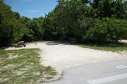 The front is open to the street. The back is filled with greenery. There is a gravel drive in the center of the site. There is a crosswalk in front of it. There is a picnic table and a fire ring on the left. Trees surround the site.